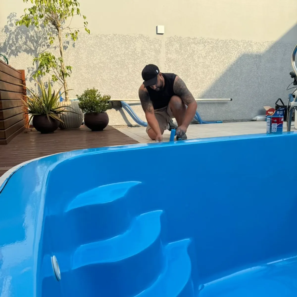 Saul trabalhando no acabamento da borda de uma piscina de fibra recém-pintada de azul.